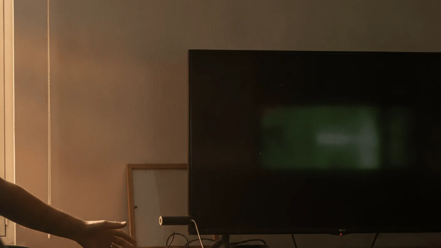 A person reaches towards a TV and streaming stick in a dimly lit living room with sunlight from a window.