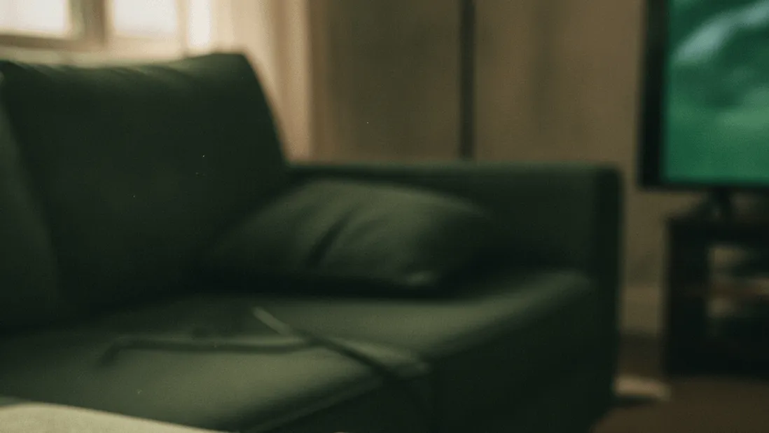 A remote control rests on a couch armrest beside a notepad with a handwritten countdown of days.