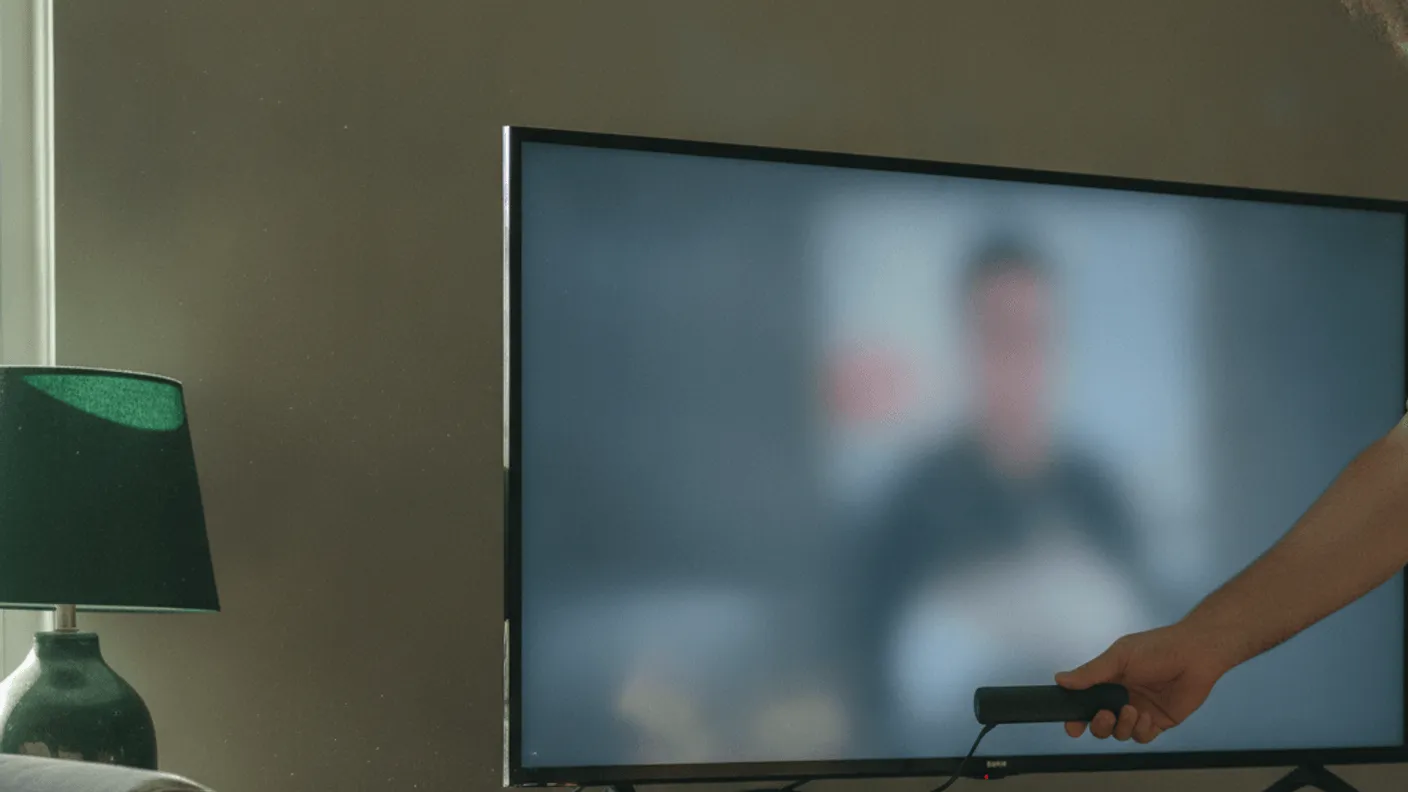 A hand inserts a streaming stick behind a television, with visible cables and a blurry screen.