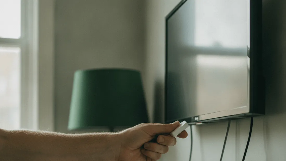 A hand inserts a streaming stick into a television, with tangled cables visible against a pale wall.