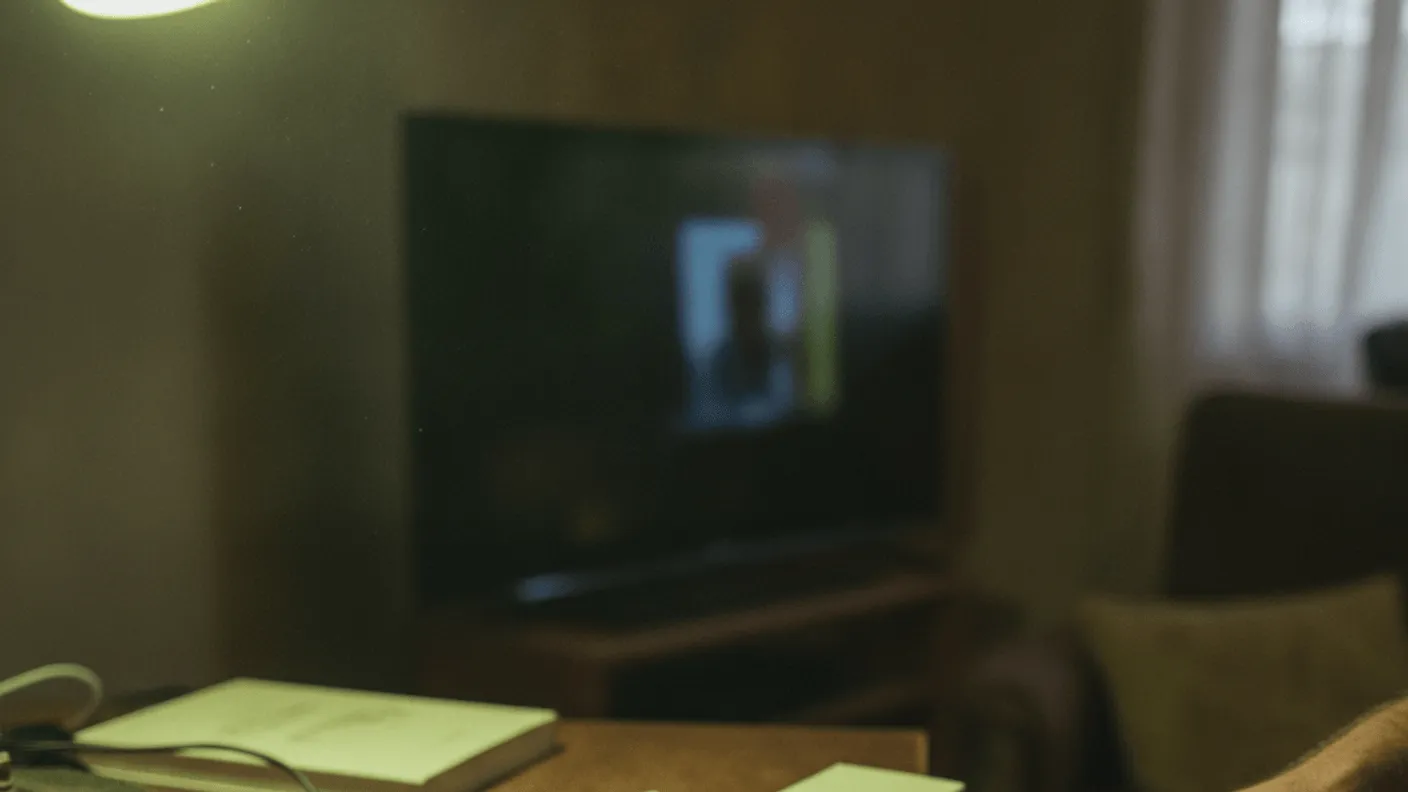 A streaming stick is being unboxed on a wooden desk with a television dimly visible in the background.