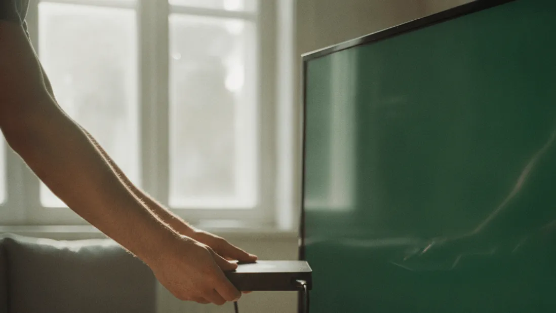 A pair of hands holds a set-top box near a television's HDMI port in an afternoon-lit room.