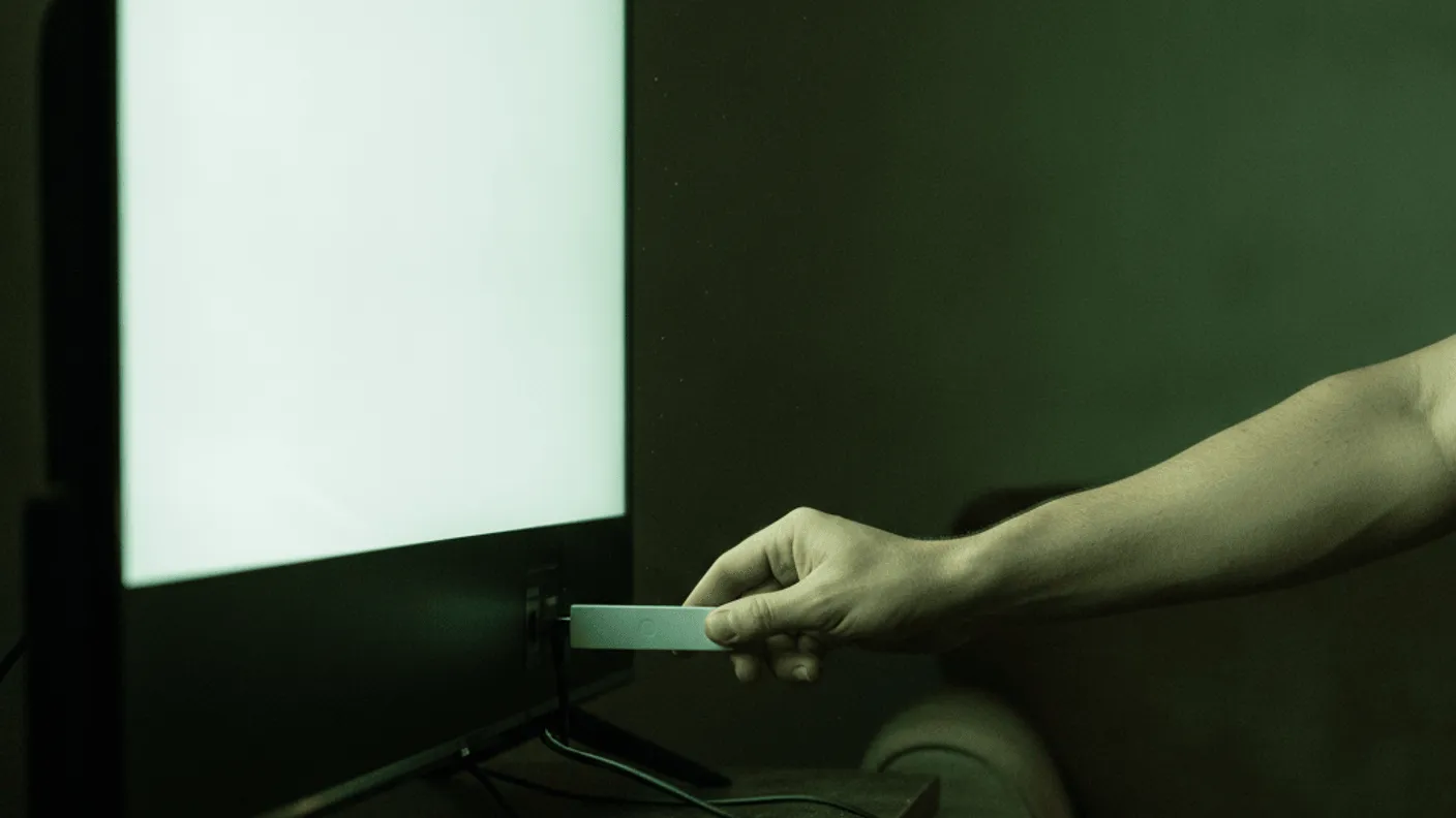 A hand inserts a streaming device into the back of a television set on a dark wood media console.